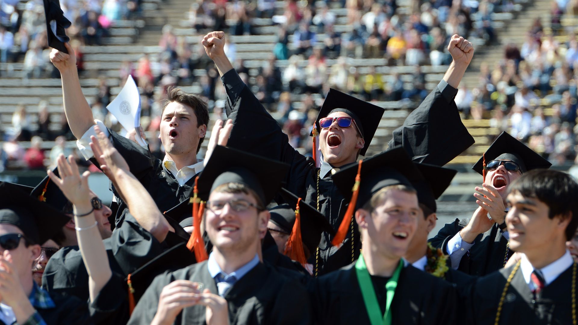 University of Colorado graduates in caps and gowns throw up their arms in celebration during Spring Commencement in Folsom Field.