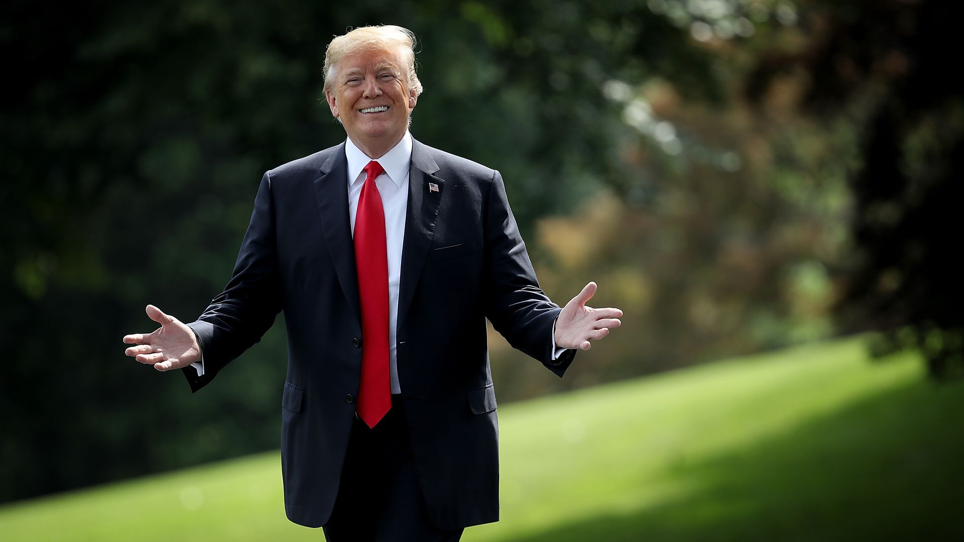 Donald Trump walking through a field wearing a dark suit and red tie
