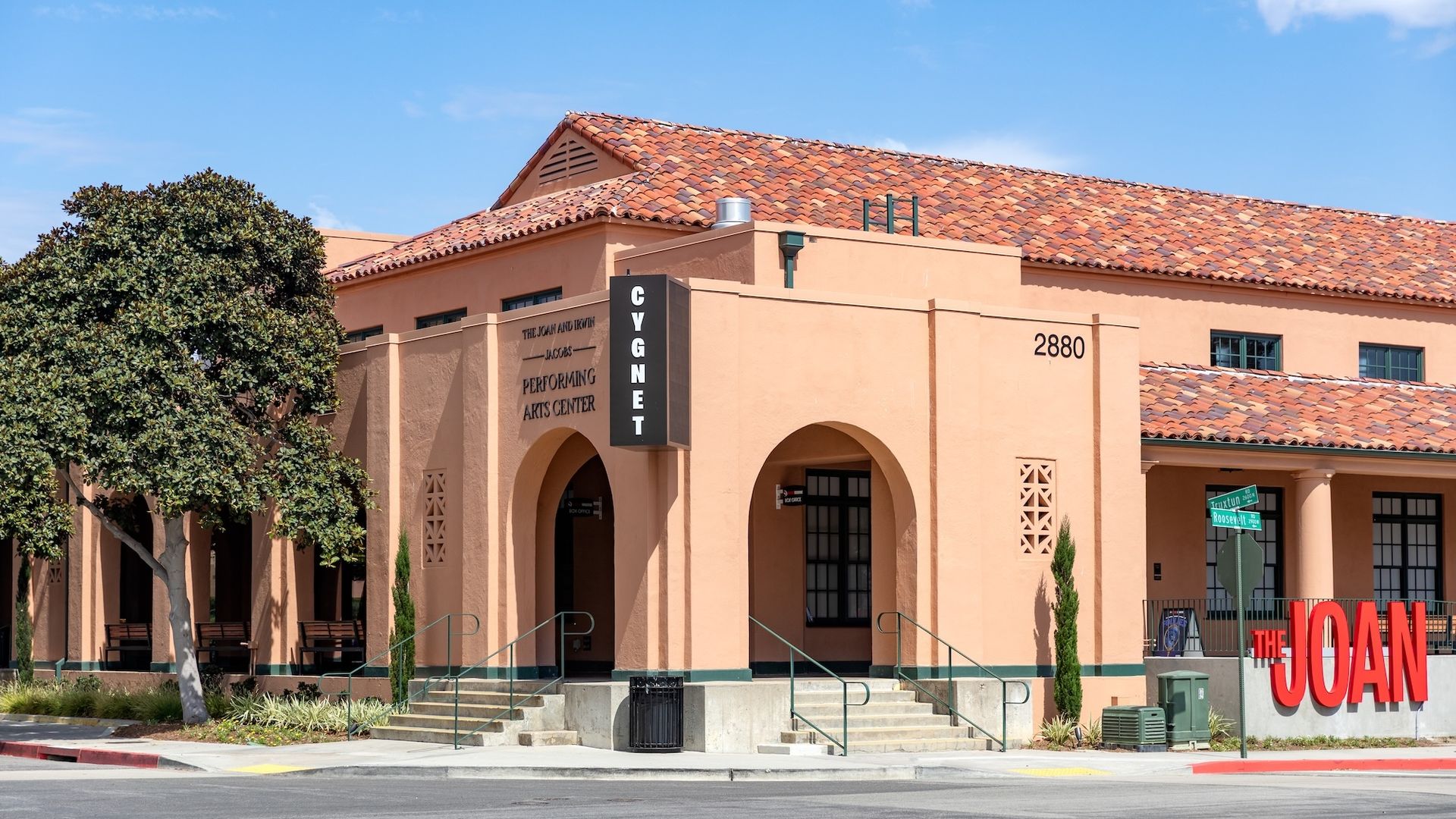 The Joan and Irwin Jacobs Performing Arts Center building with peach-colored walls, terracotta tile roof, large red "THE JOAN" sign.
