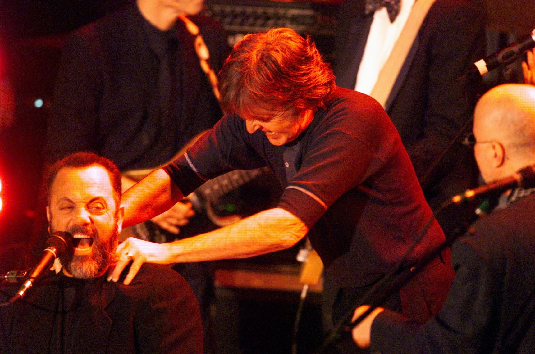 Paul McCartney playfully grabs Billy Joel's shoulders as they perform on stage. 