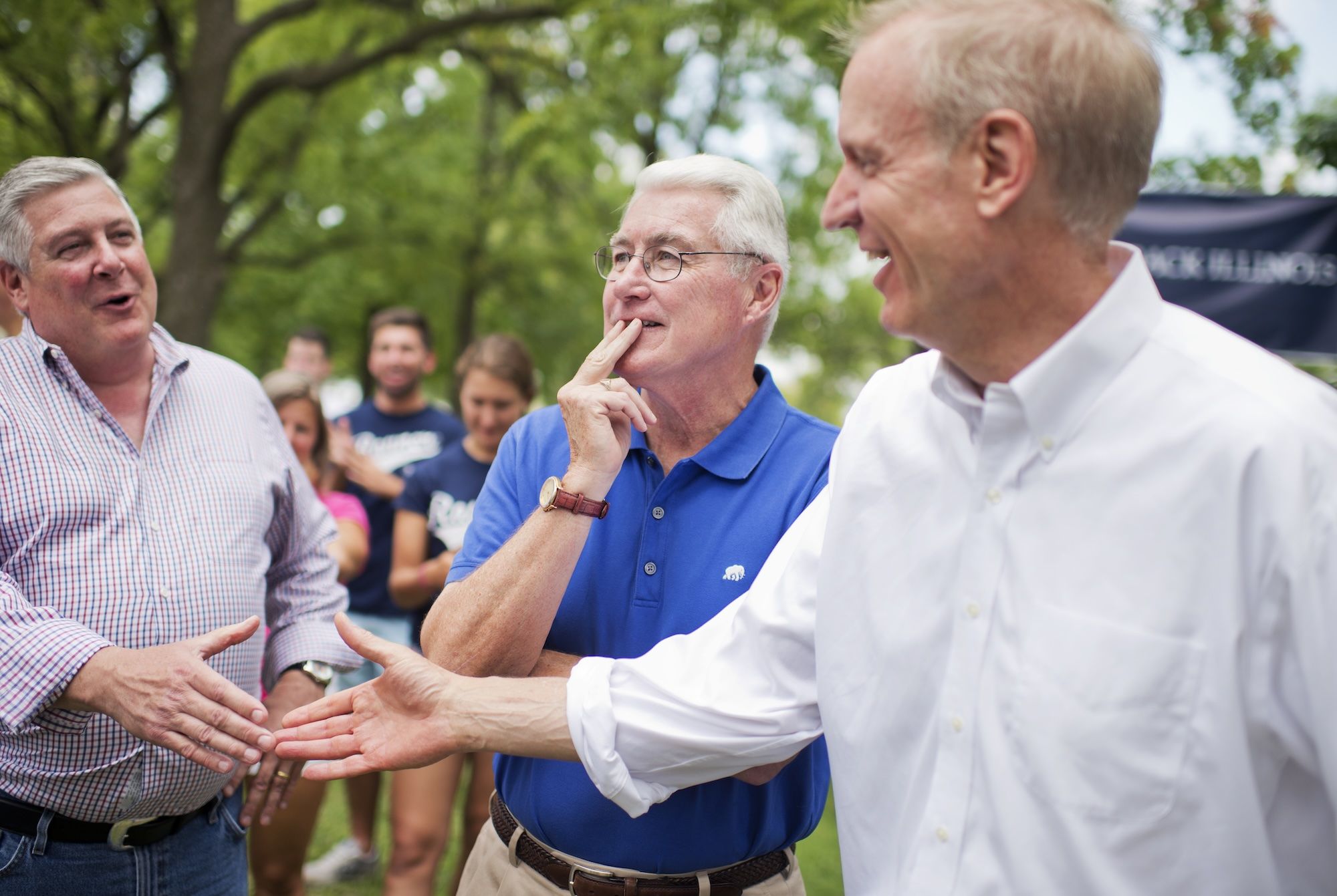 Kirk Dillard in striped button down, Jim Edgar in blue polo shirt and Bruce Rauner in white button down. Dillard and Rauner extending their hands to shake.