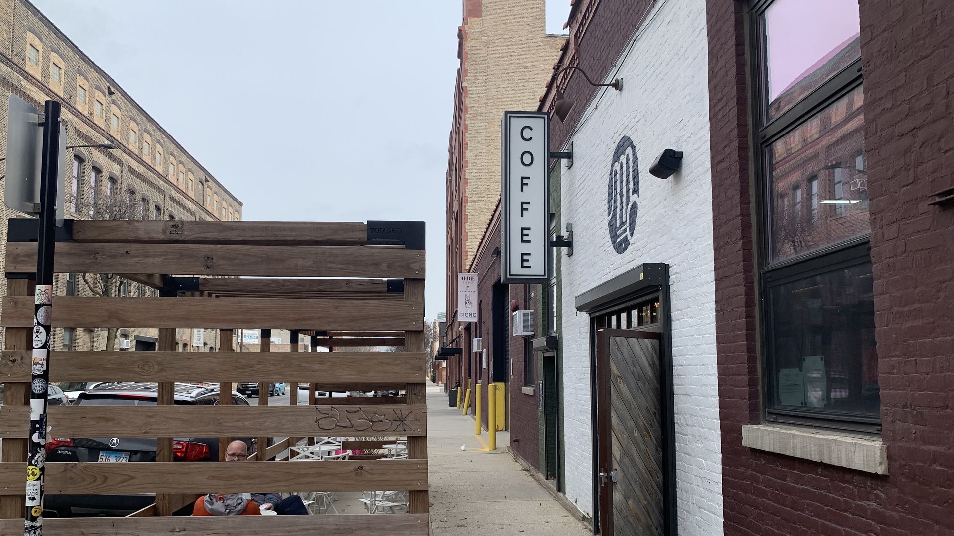 White brick building with sign reading "Coffee" with wood patio out front.