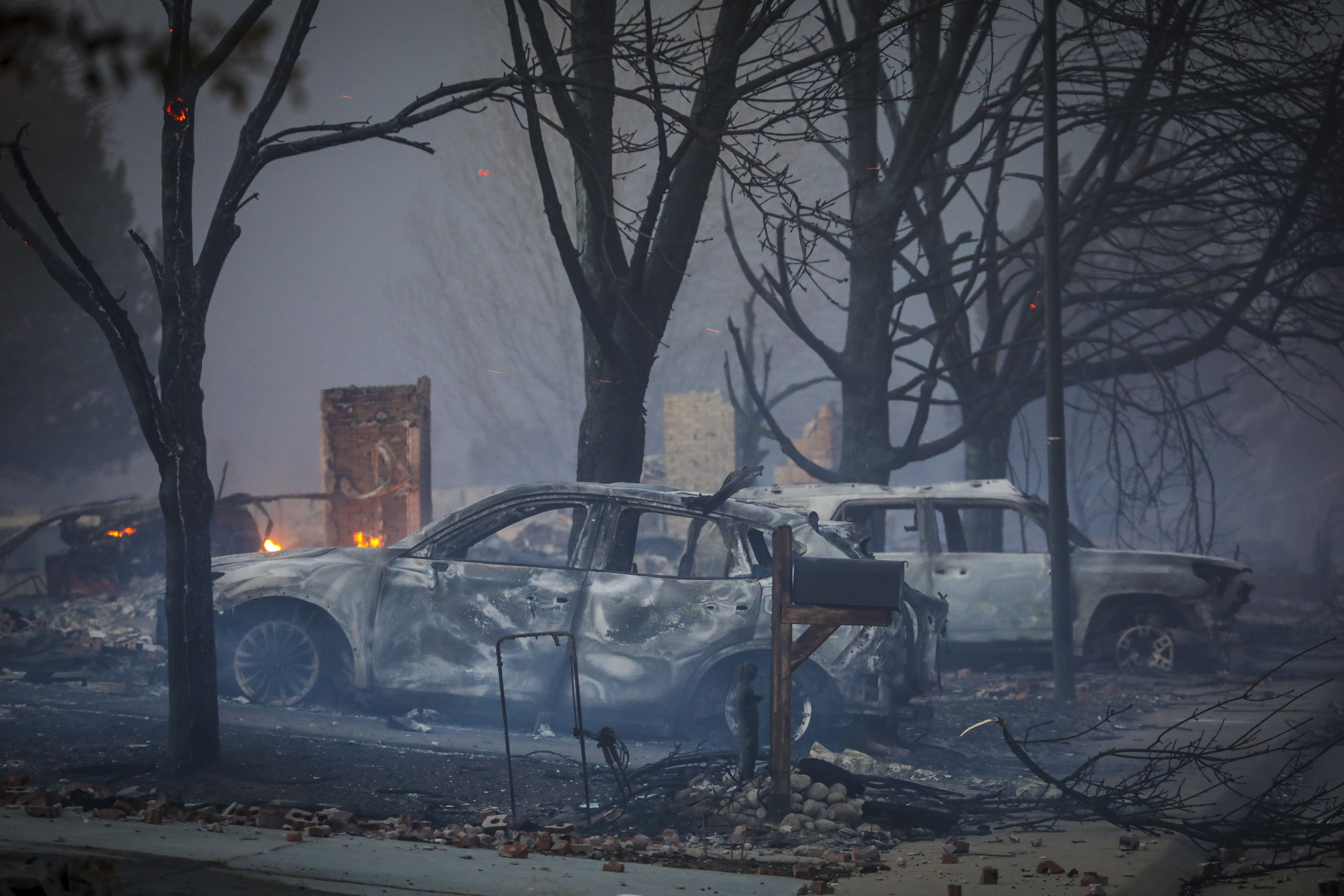 Burnt out vehicles sit amidst the smoke and haze after a fast moving wildfire swept through the area.