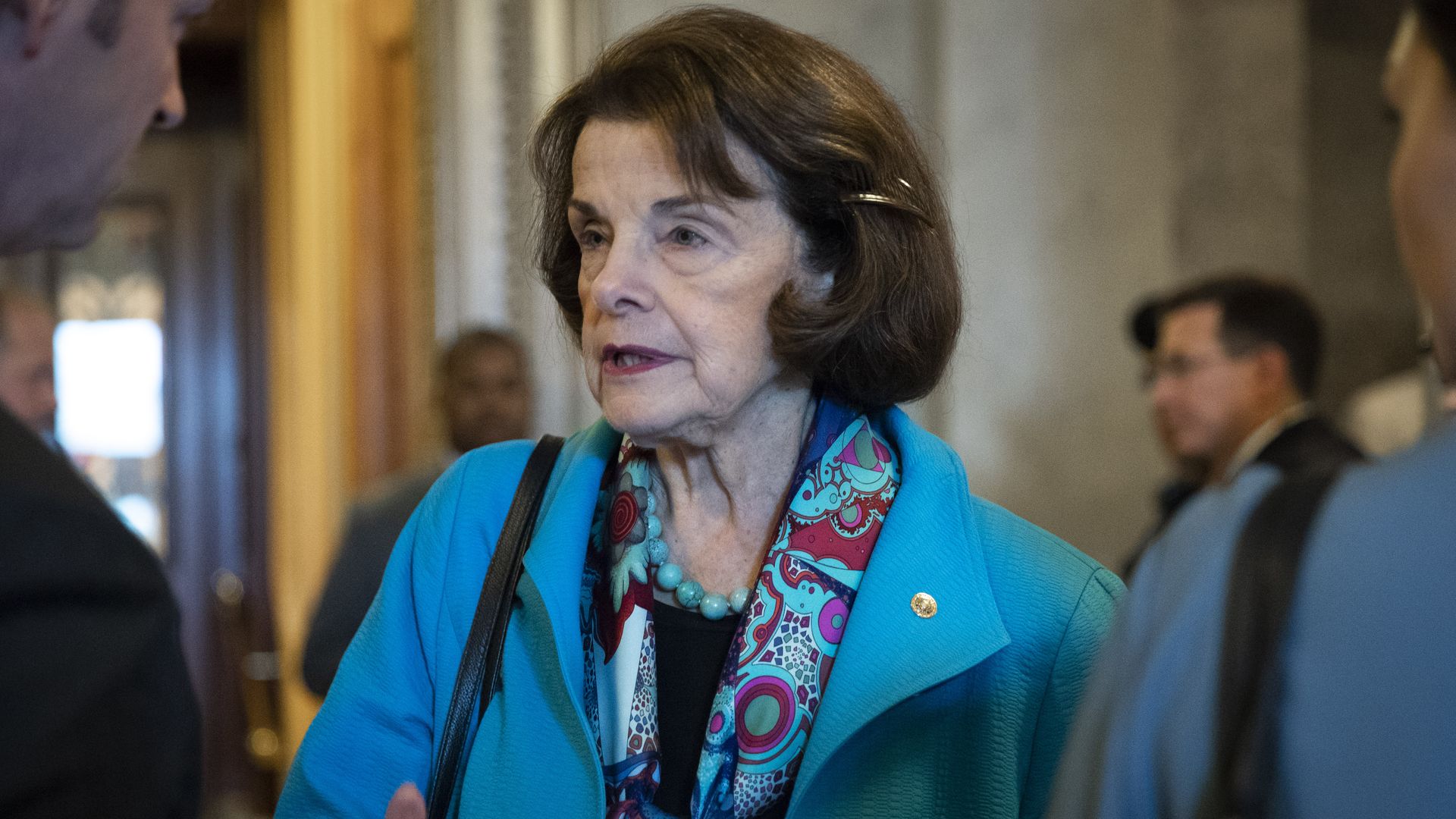 In this image, Dianne Feinstein wears a bright blue coat and speaks to reporters. 