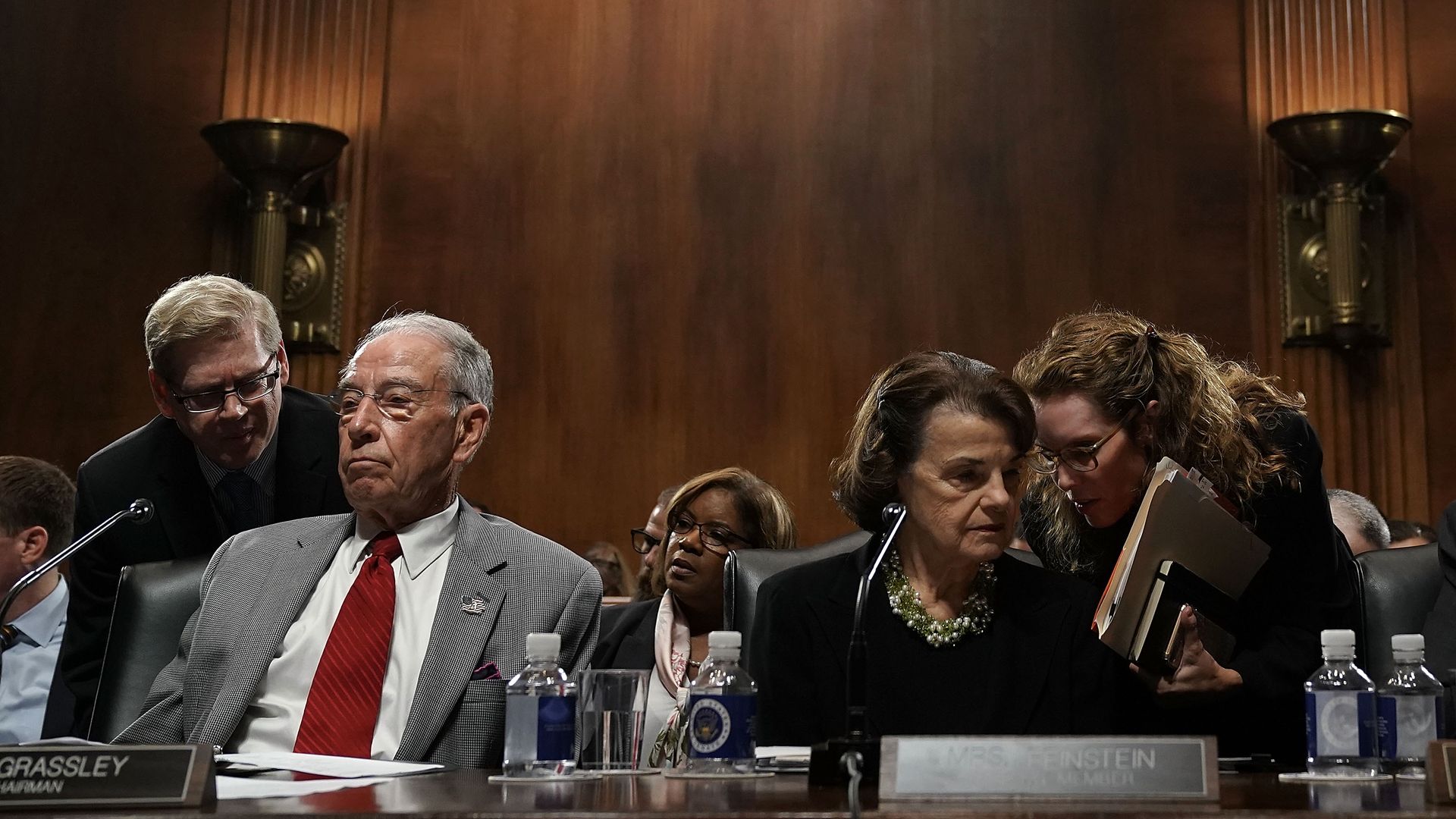 Chuck Grassley and Dianne Feinstein talking to their aides in a briefing room. 