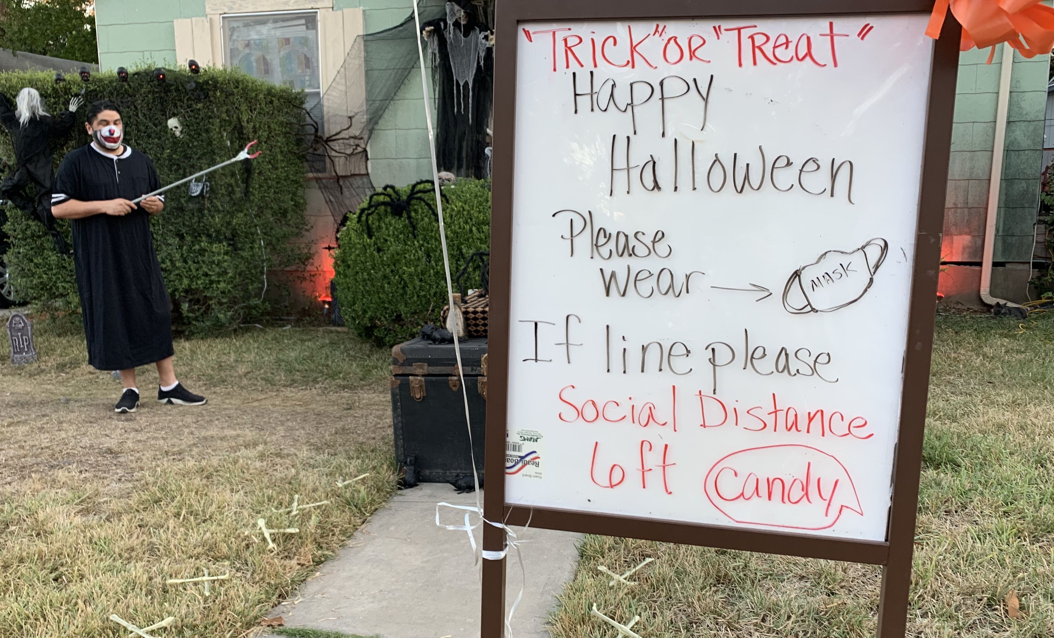 A man stands behind a sign asking trick-or-treaters to social distance.