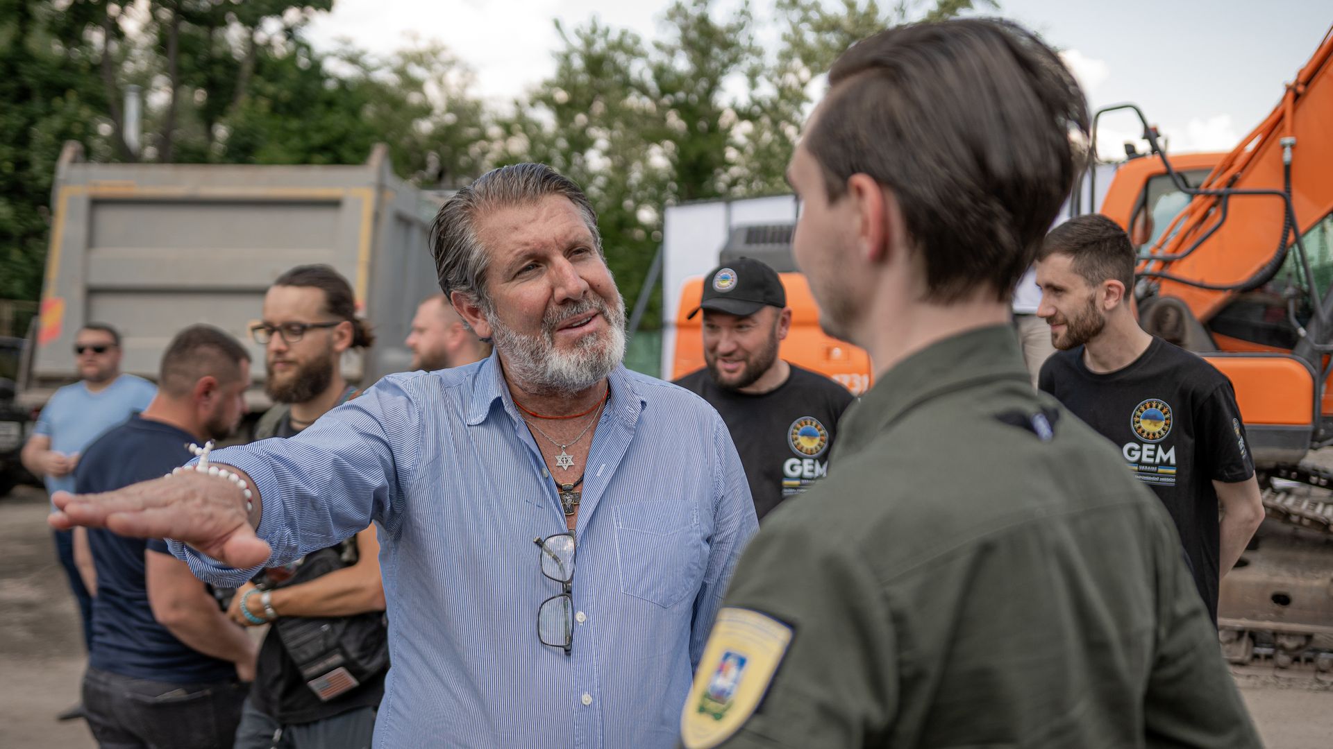 A man in a blue button-down shirt gestures to a man in green military fatigues. 