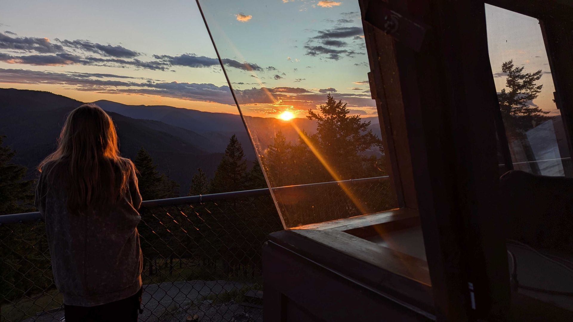 A girl looks at a sunset from a balcony of a glass building.