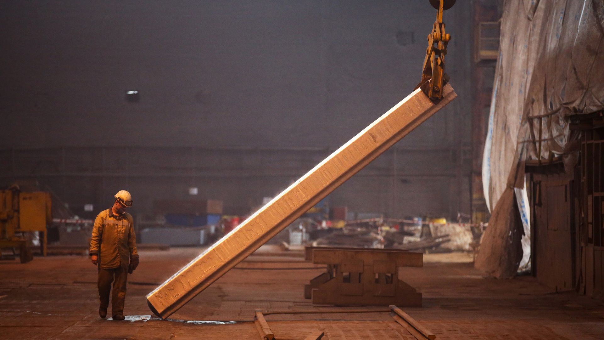 A worker watches an aluminum slab being lifted.
