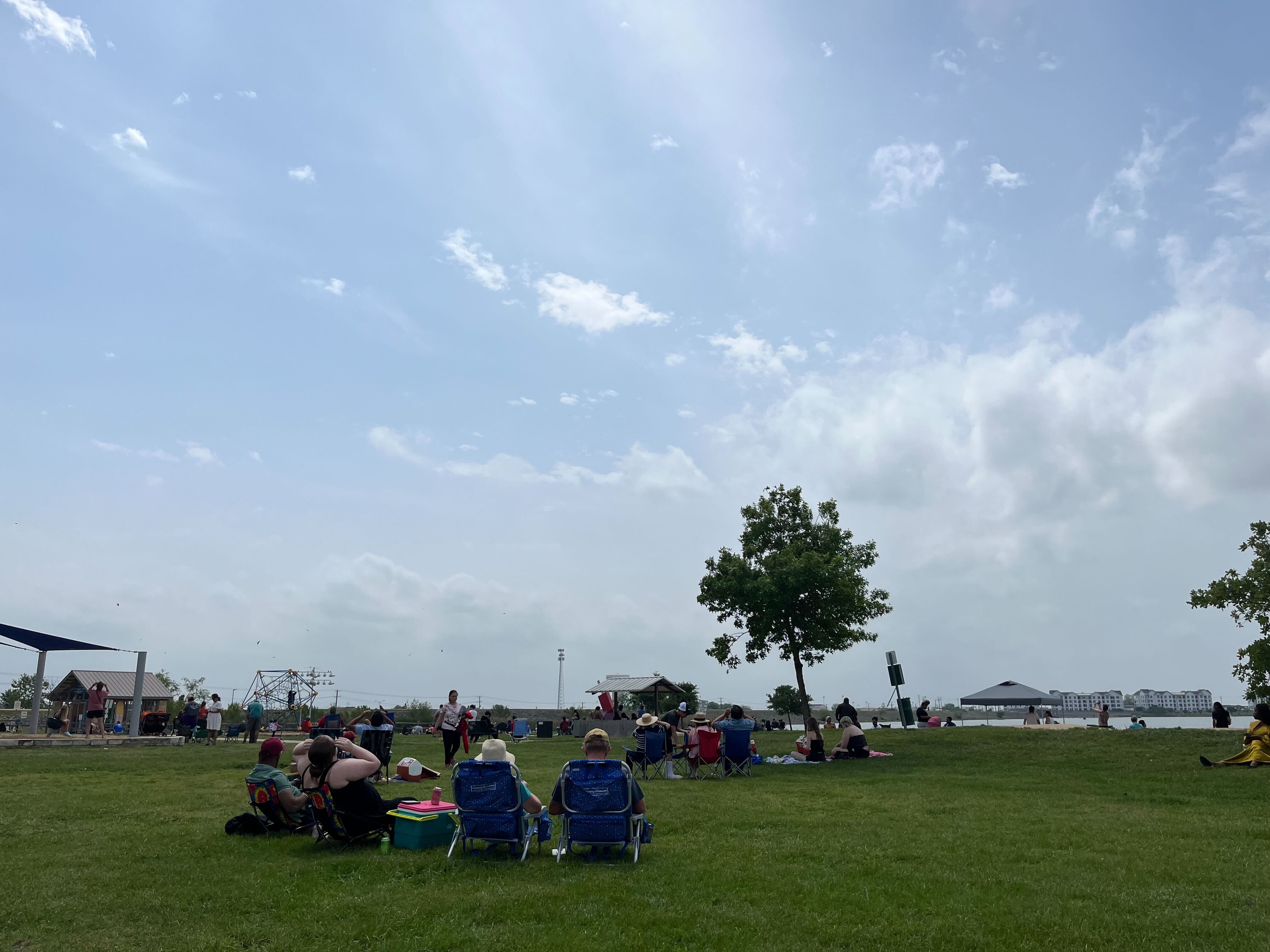 Several people sit in a field looking up at the sky