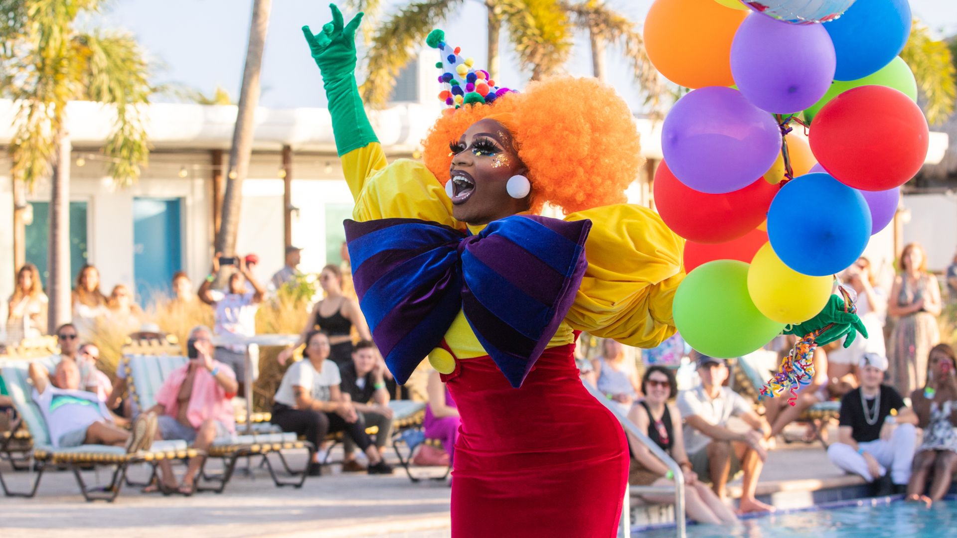 A drag queen dressed as a clown holding balloons