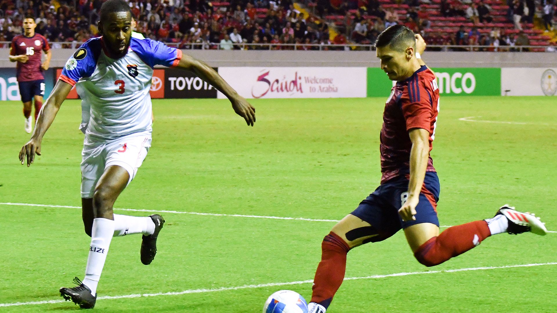 A photo showing a Belize defender playing a Costa Rican defender who is moving to kick a soccer ball