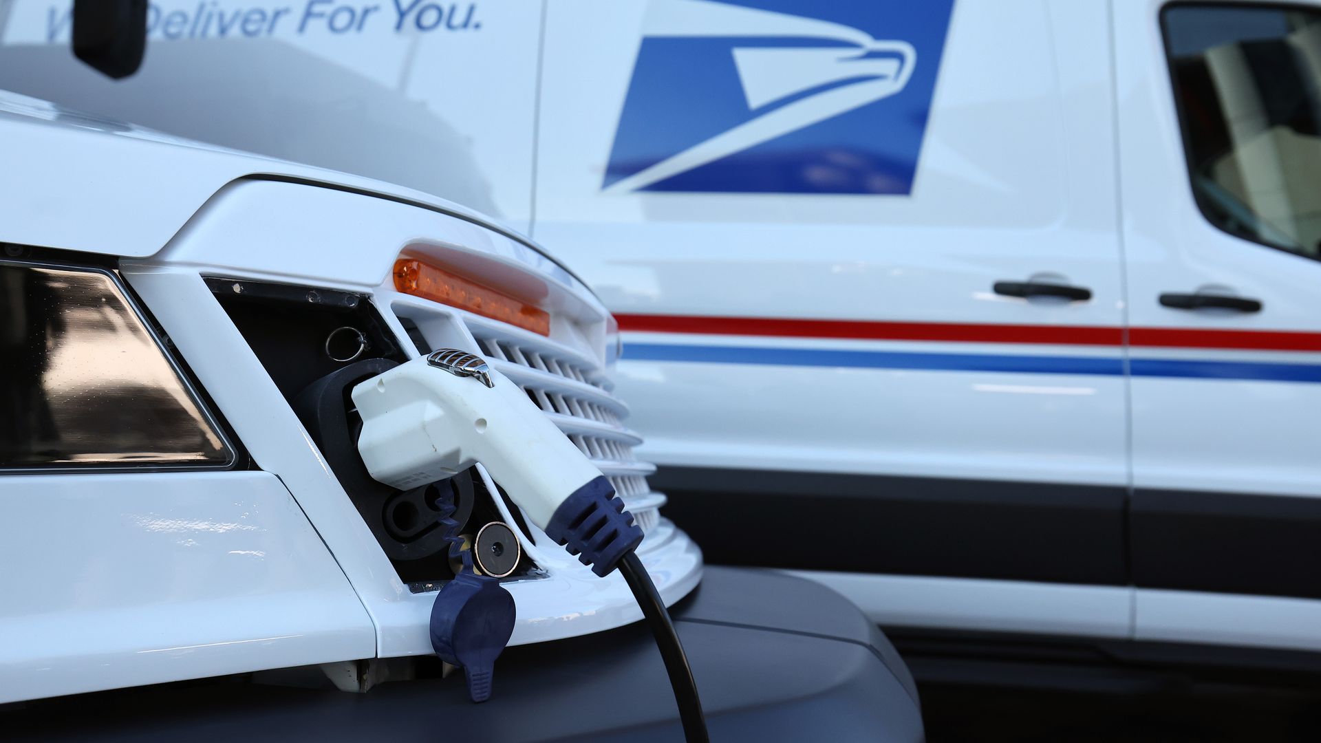 A United States Postal Service electric delivery vehicle, plugged into a charging station. 
