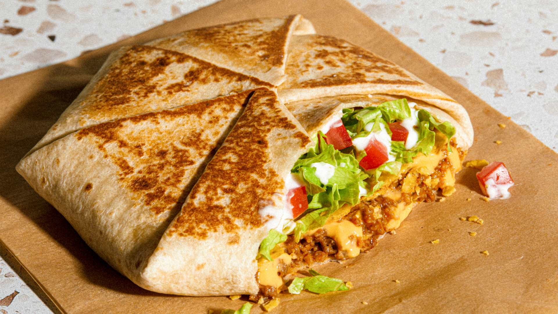A Crunchwrap Supreme cut into six triangles with beef, cheese, lettuce and tomatoes falling out.