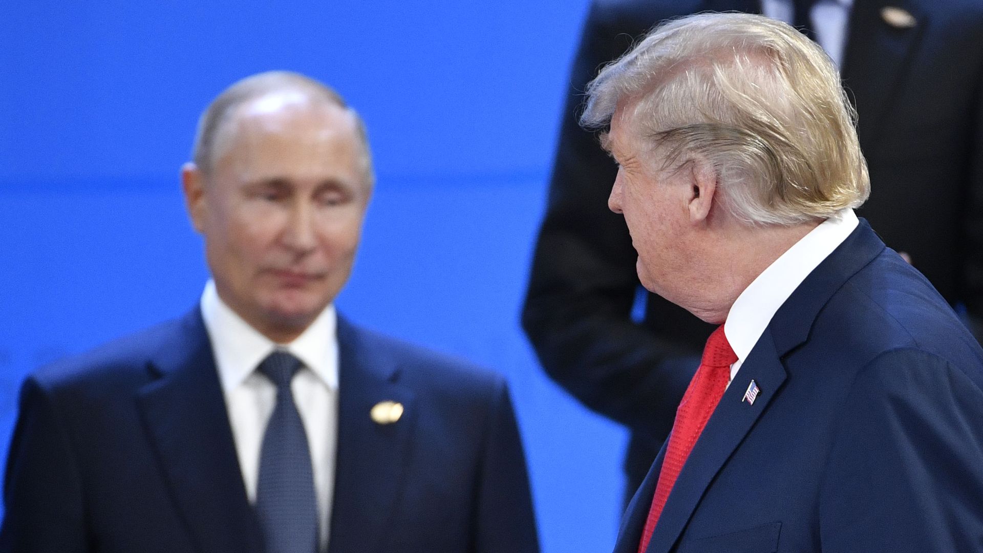 In this image, Trump walks by Putin and smiles at him.
