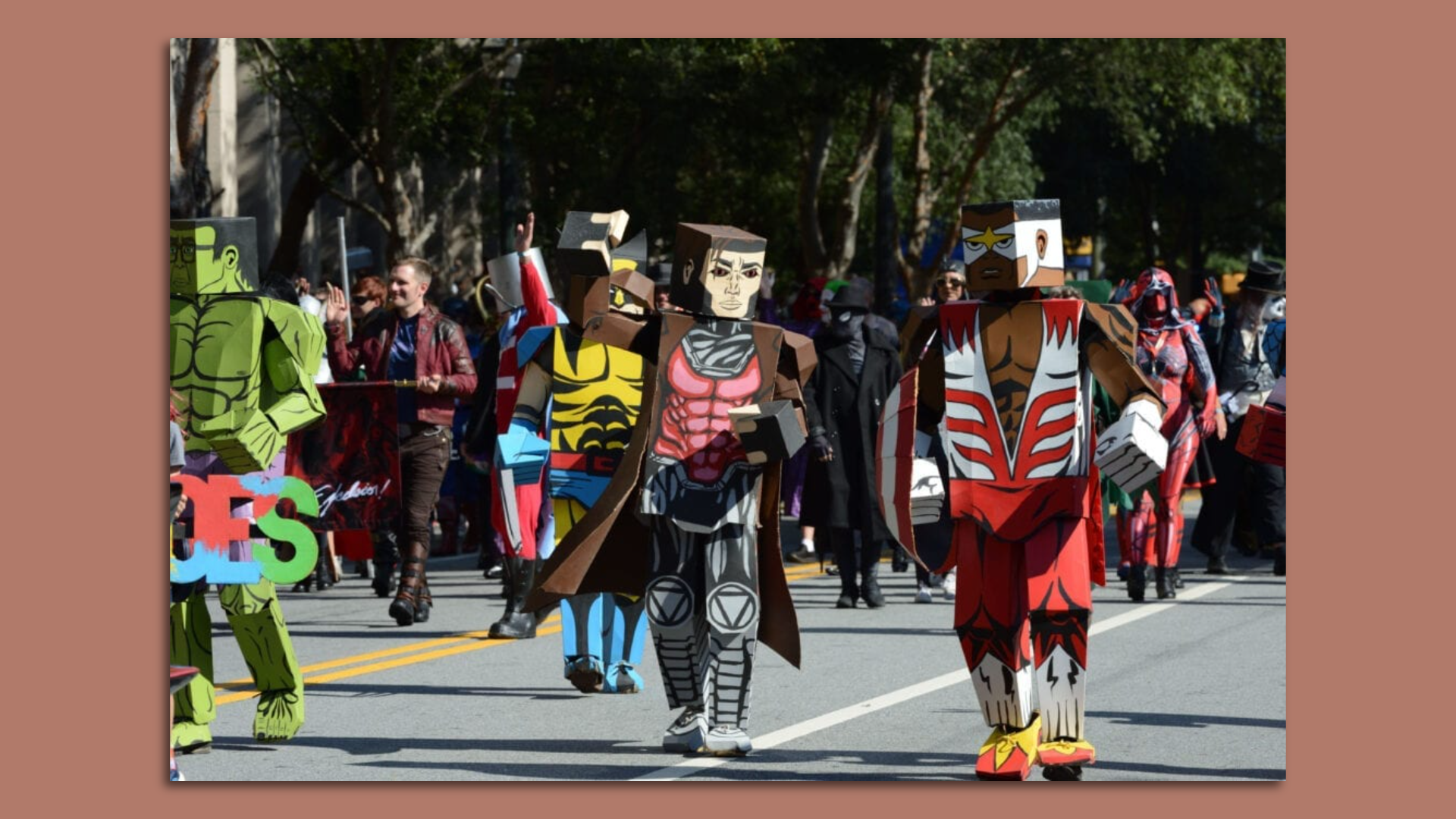 Individuals dressed as Marvel super heroes in block-shaped costumes walk in a parade