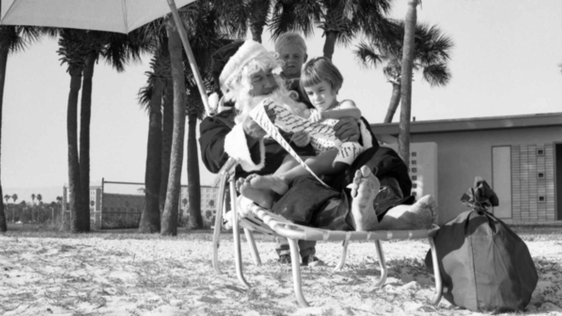 A man dressed as Santa Claus with children in his lap on a chair on the beach.