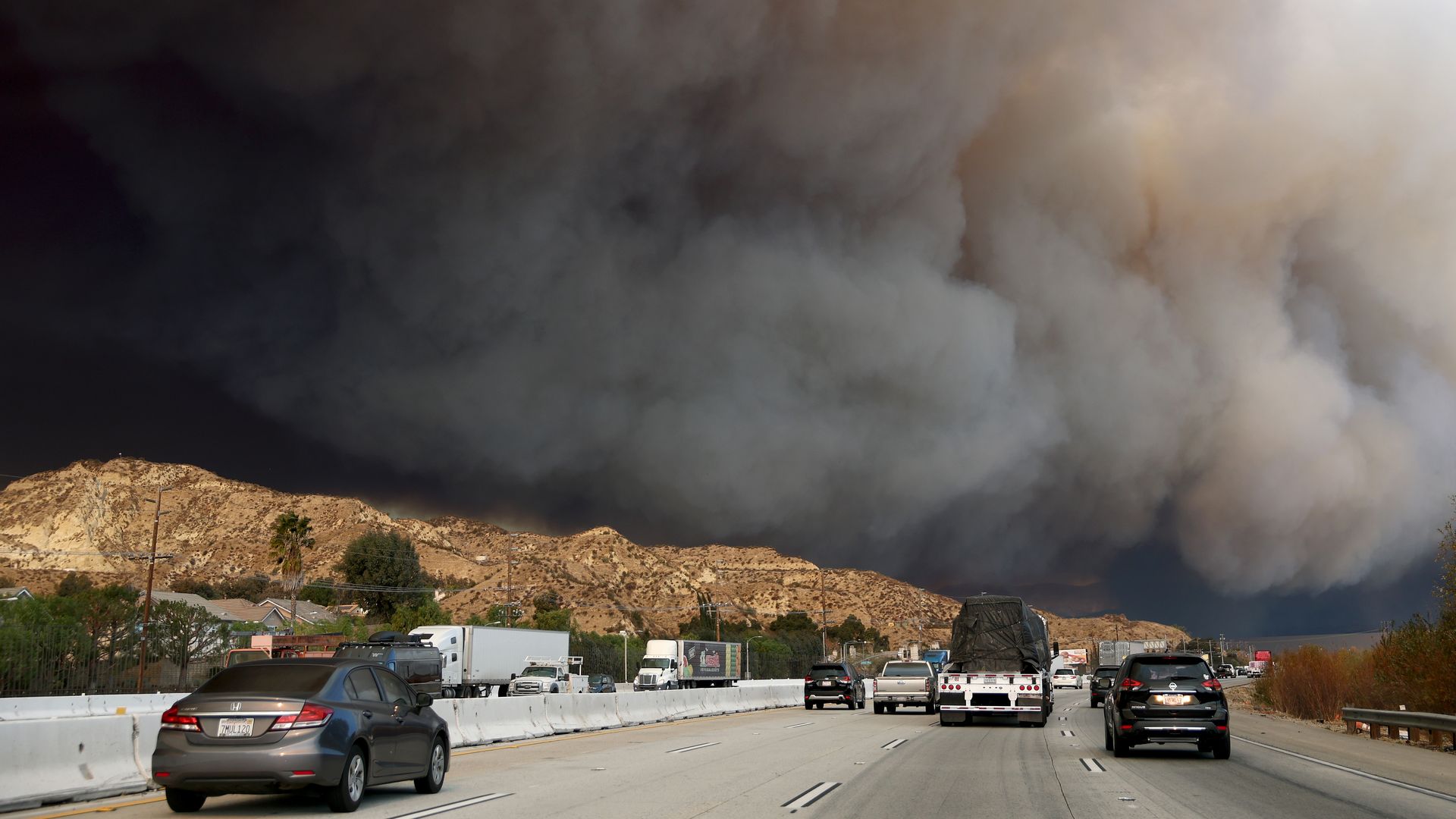 A photo of cars on a highway driving towards thick, dark wildfire smoke.