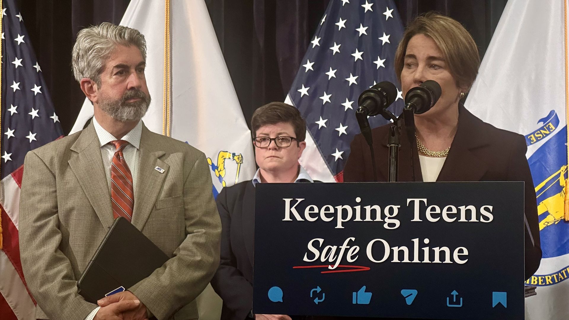 From left, Massachusetts Teachers Association president Max Page stands next to Gov. Maura Healey as she speaks from a lectern that says "Keeping Teens Safe Online" during a press conference.