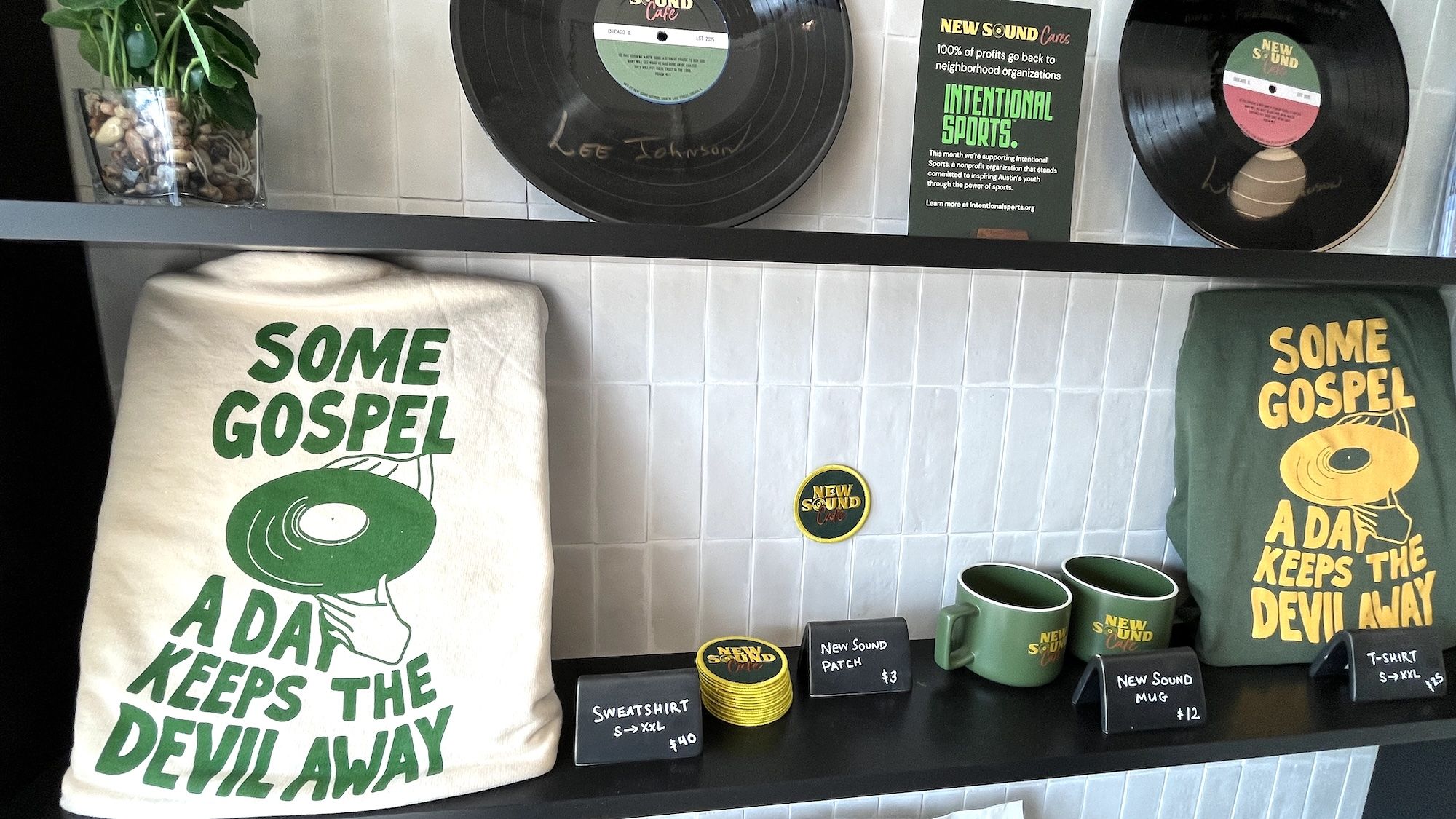 A retail shelf displays two T-shirts printed with the slogan "SOME GOSPEL A DAY KEEPS THE DEVIL AWAY", green mugs, a circular "New Sound" badge, vinyl records, a plant, and price tags.
