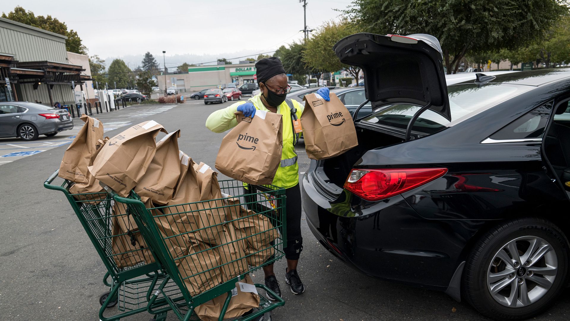 An Amazon worker puts bags of groceries into the trunk of a car.