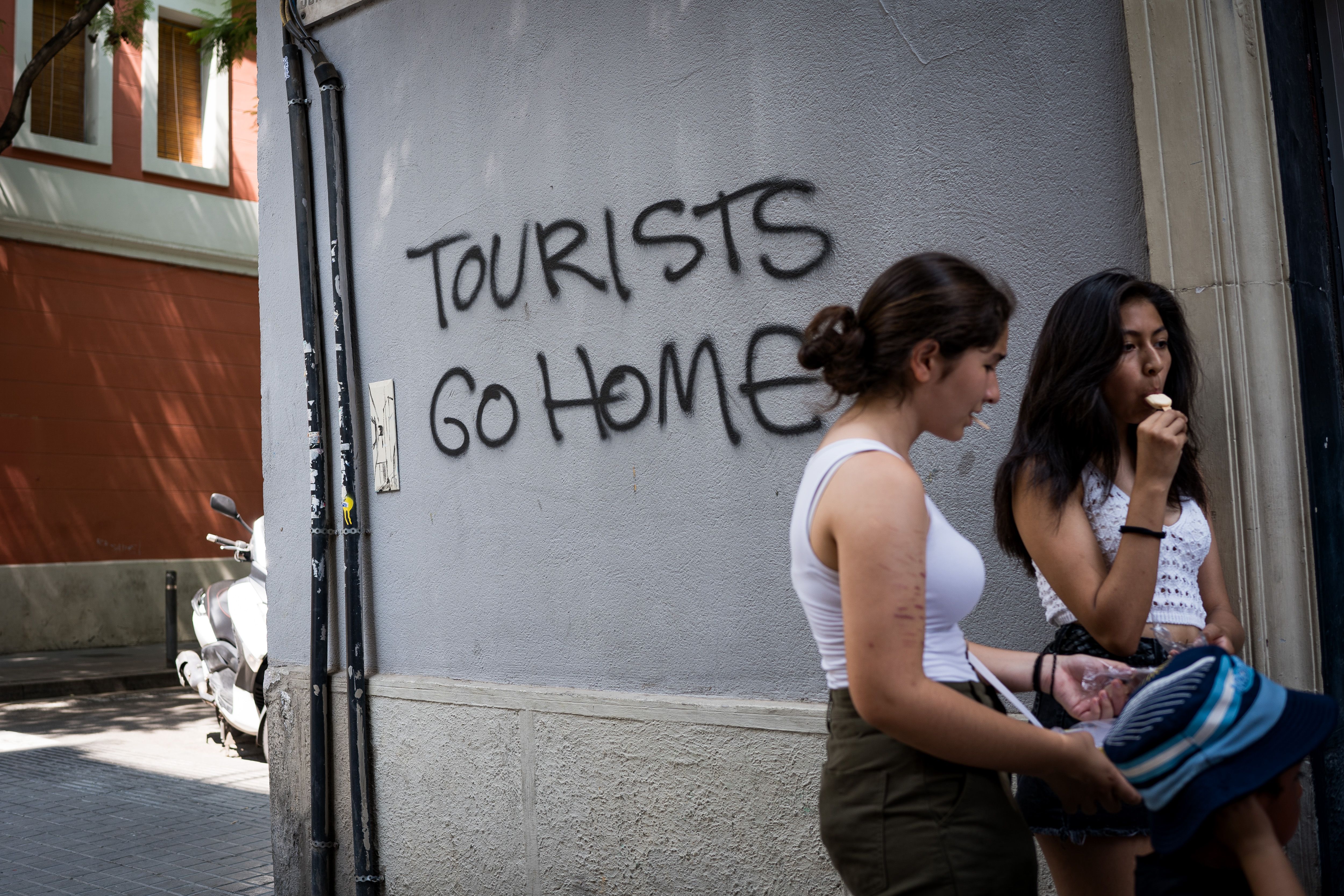 BARCELONA, SPAIN - 2024/08/21: People seen next to a graffiti reading "tourists go home" on a wall in the city center. With more than 18 million tourists expected to visit Barcelona in 2024, the city is struggling to find a balance between the economic benefits of tourism during the tourist season, 