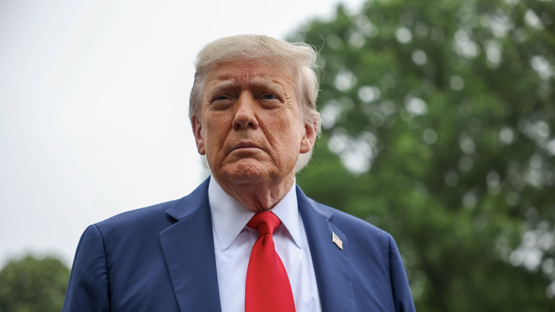 President Trump looks on in a navy blue suit and a red tie.