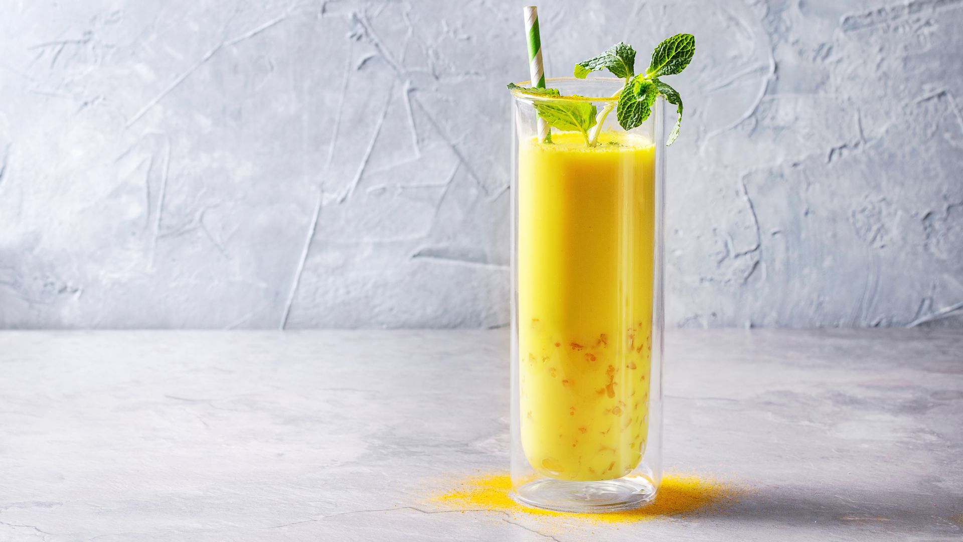 A tall glass holding a bright yellow drink on a marble table