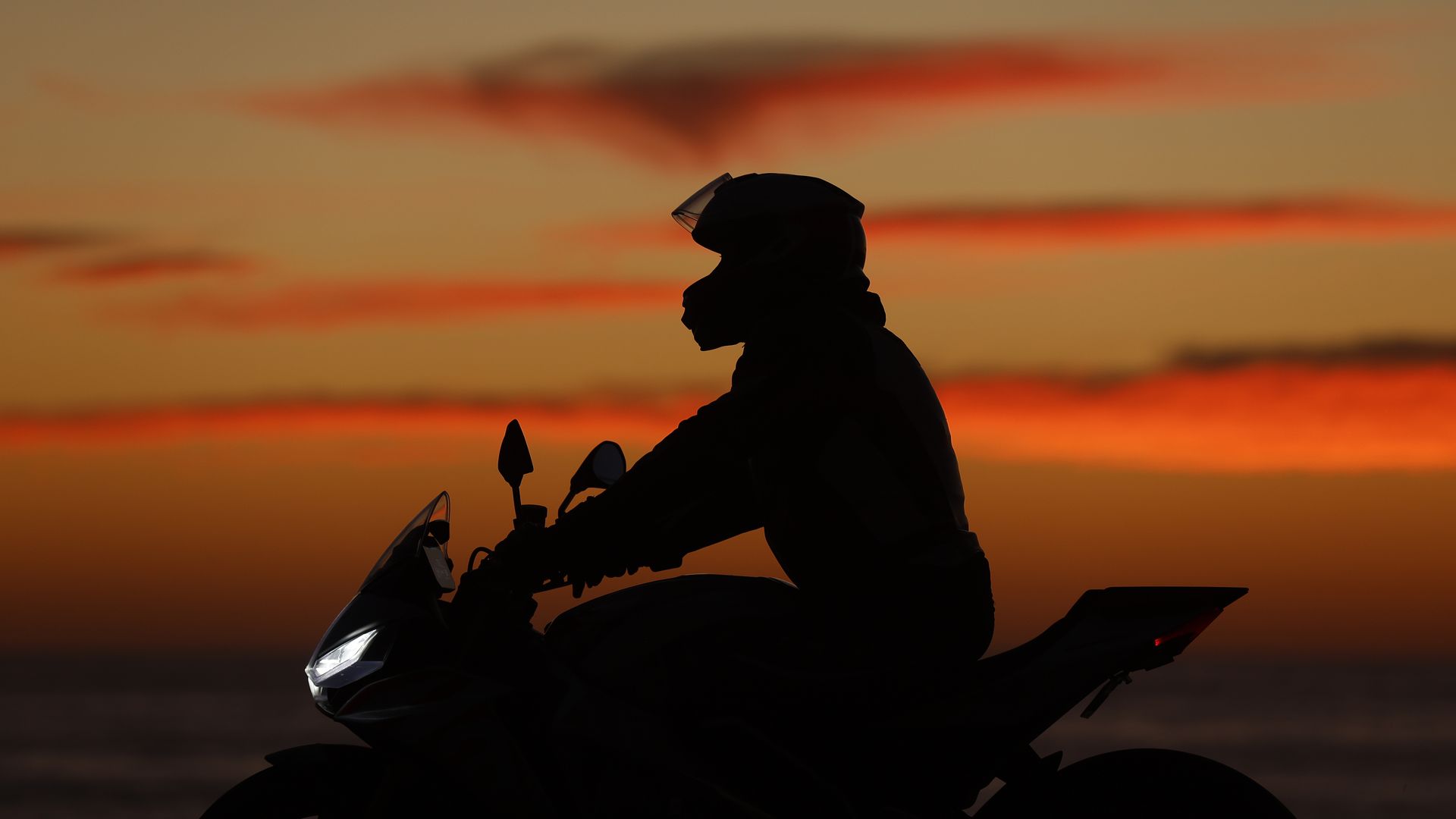 A motorcyclist is seen riding in silhouette against a sunset. 