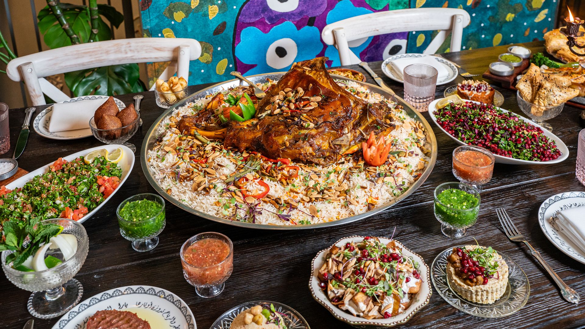 A table filled with dishes of food including lamb shank, salads, and  green drinks