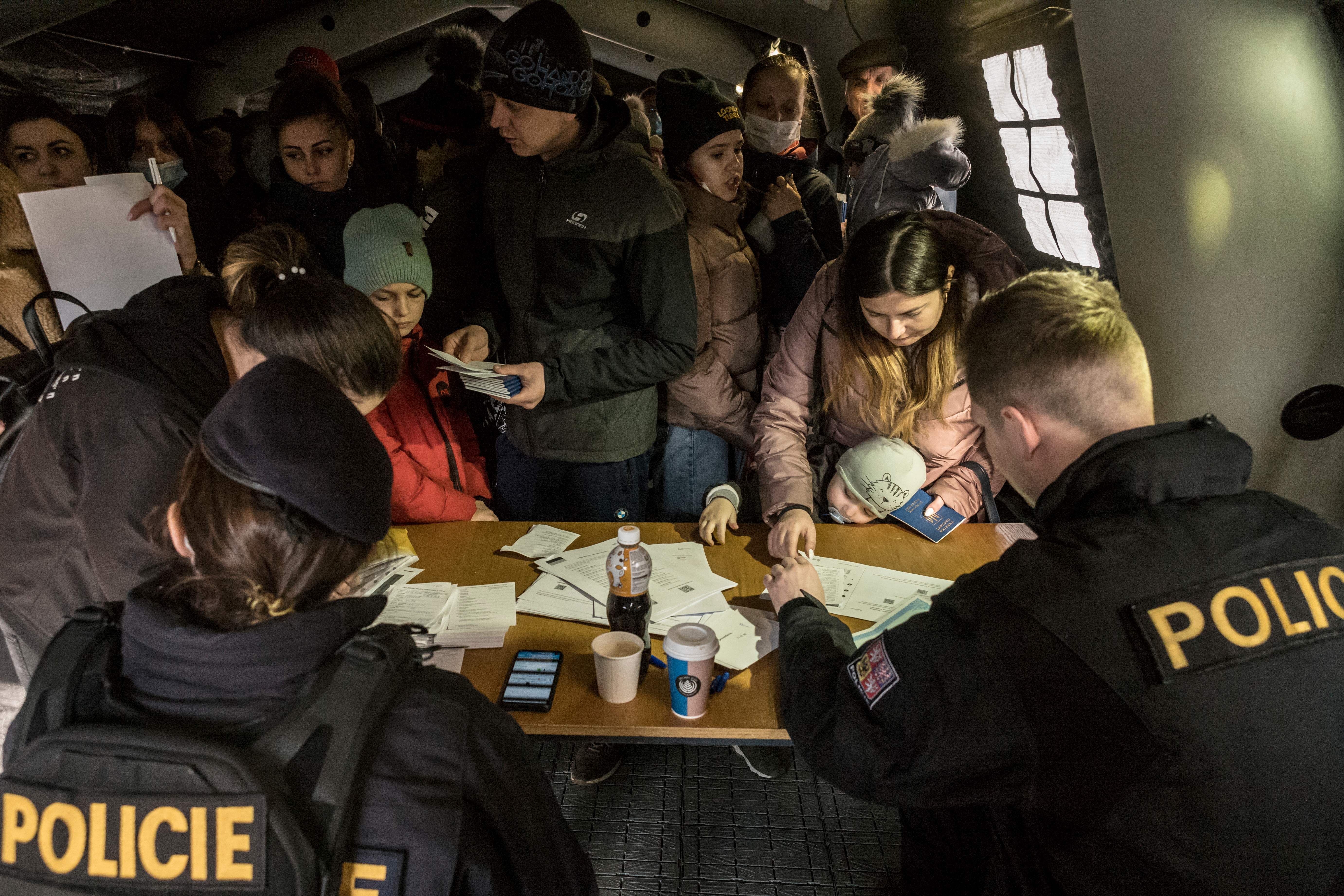 Photo of people crowded into a tent and standing before two police officers with documents on the table