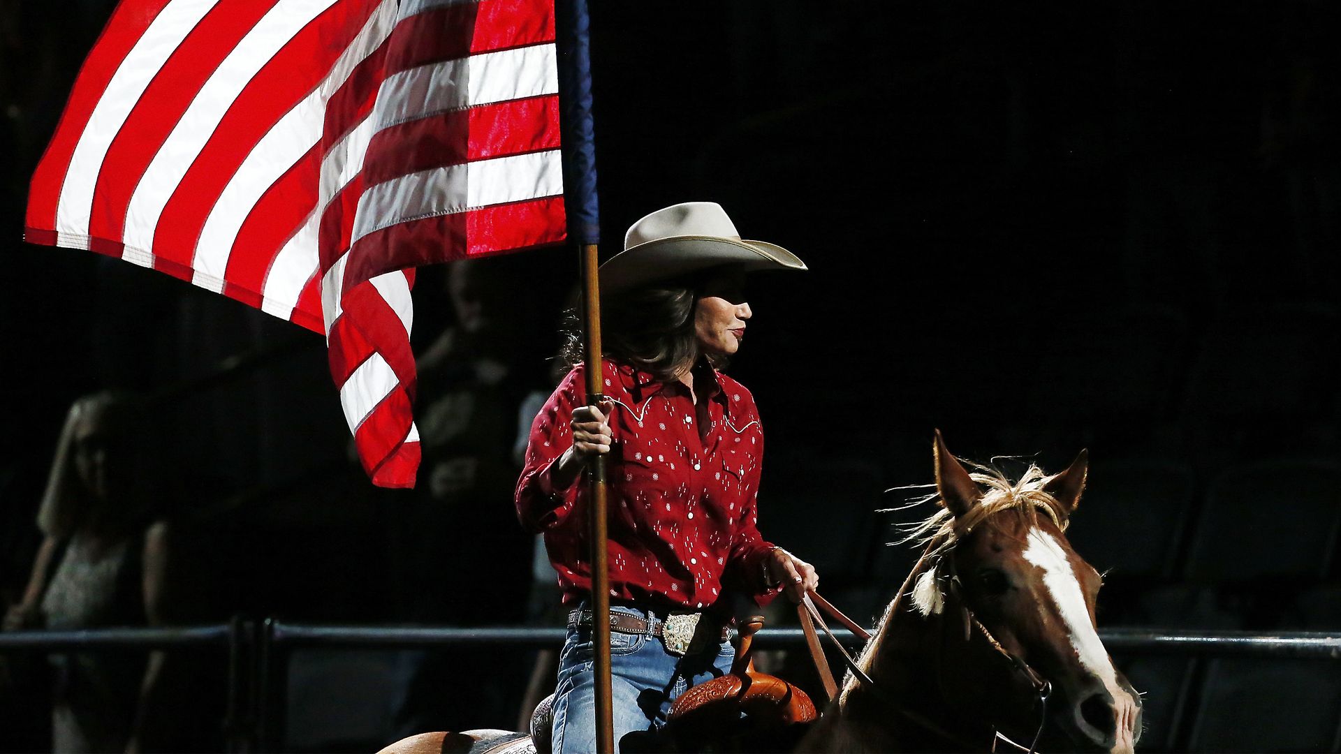 South Dakota Governor Kristi Noem carries a large American flag while riding a horse