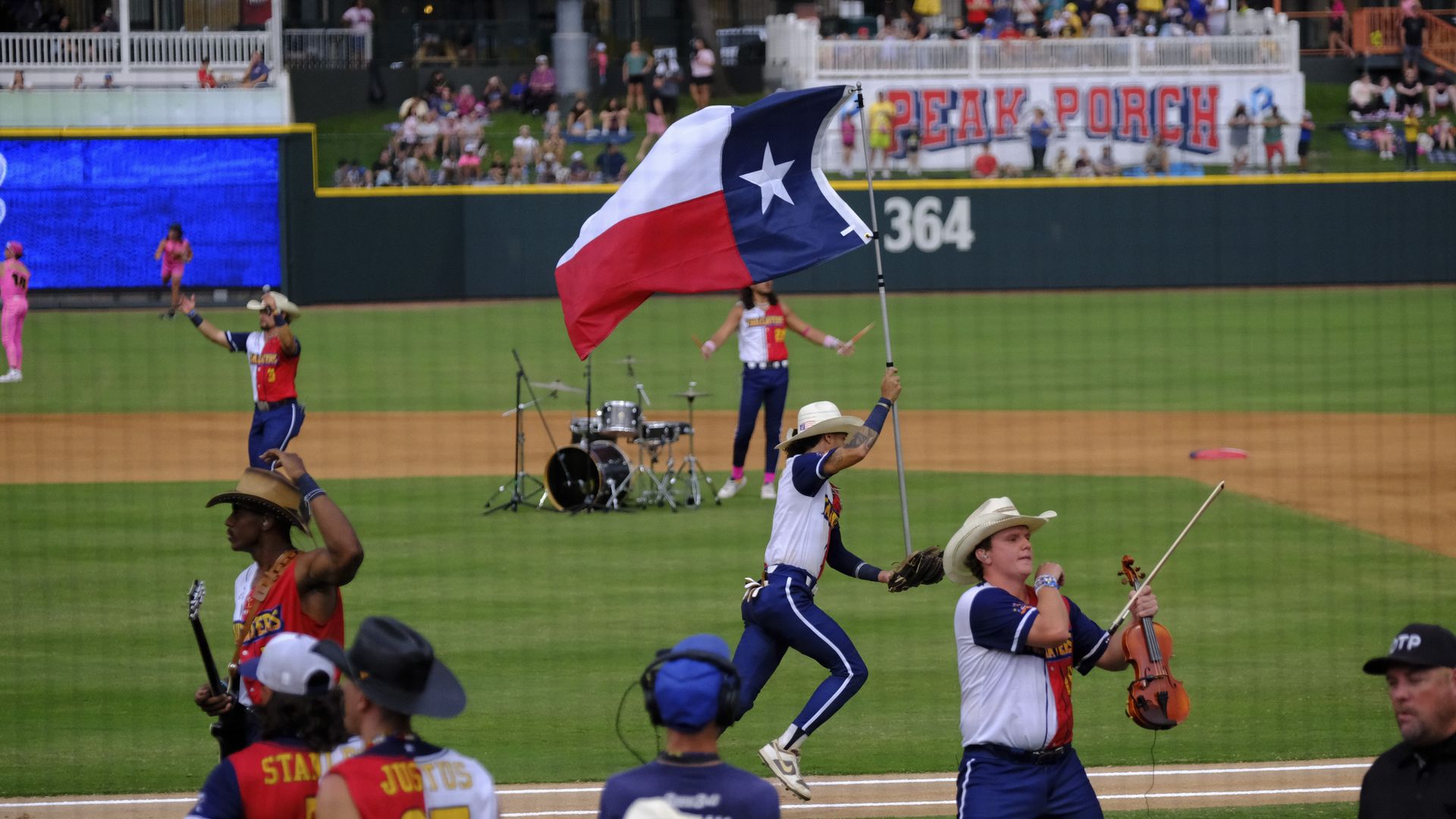 The Texas Tailgaters wearing red, blue and white uniforms wave a Texas flag on a ballfield. 