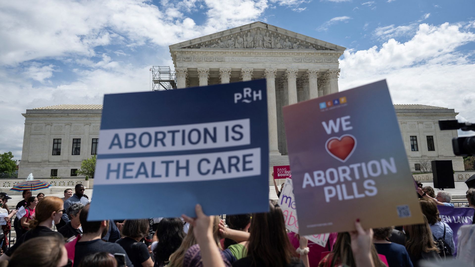 Picture of an abortion rights protests outside of the Supreme Court, and two signs say "abortion is health care" and "we love abortion pills"