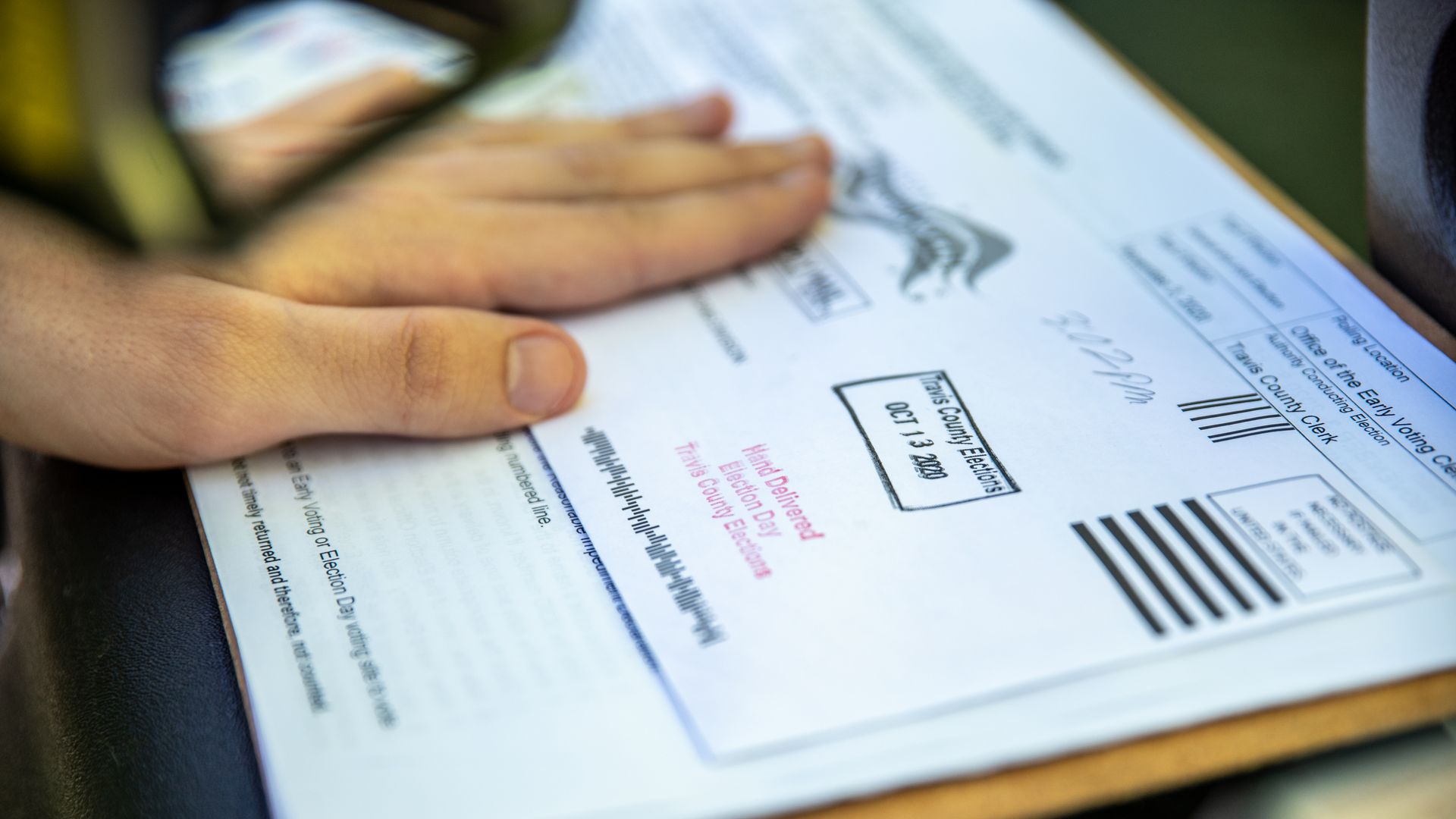 Photo of a hand covering a ballot about to be submitted