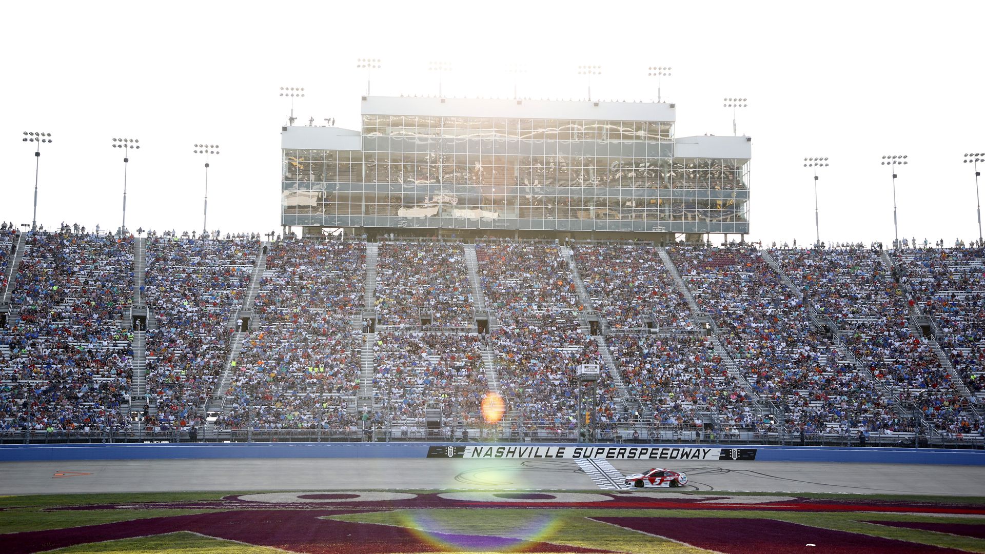 race car drives on track with sun shining above