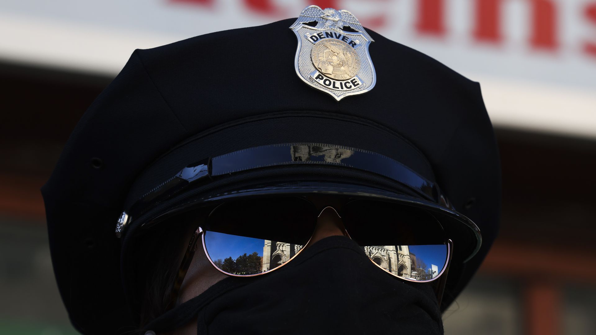 A close-up photo of a police officer wearing a uniform hat, sunglasses and COVID-19 mask.