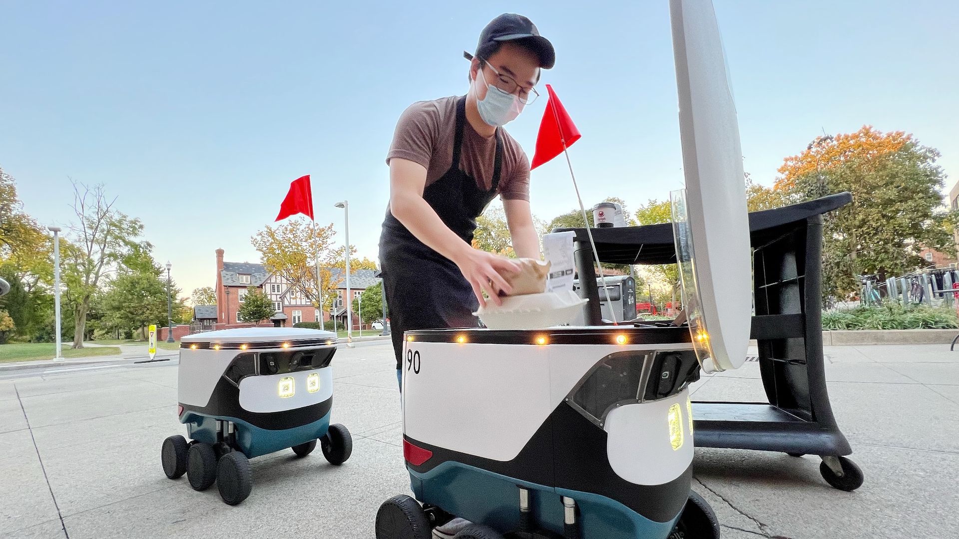 A restaurant worker loads a delivery robot with food.