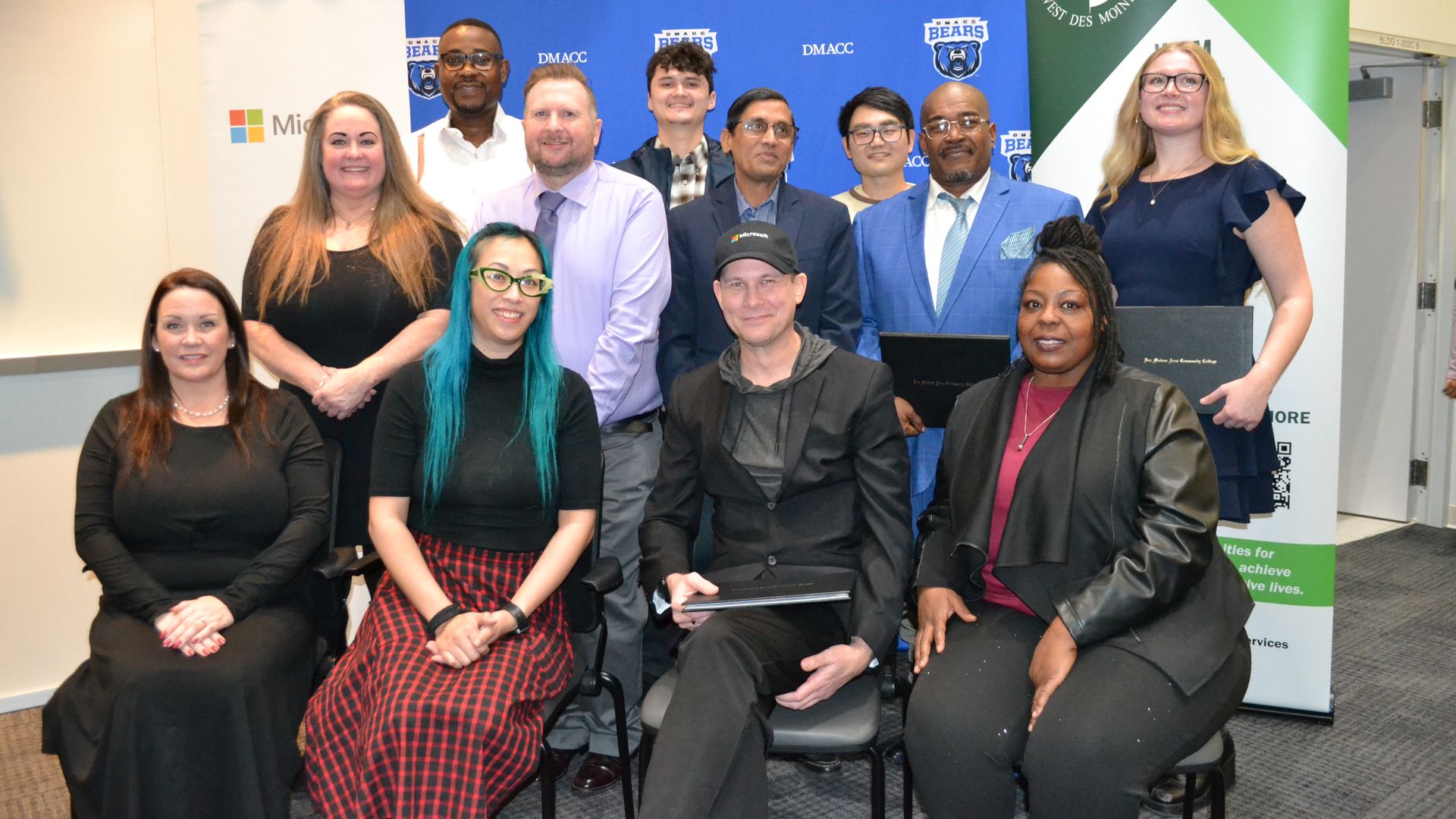Group portrait of diverse professionals posing in front of a blue DMACC Bears backdrop and a green West Des Moines banner; several seated in front, others standing behind, smiling.