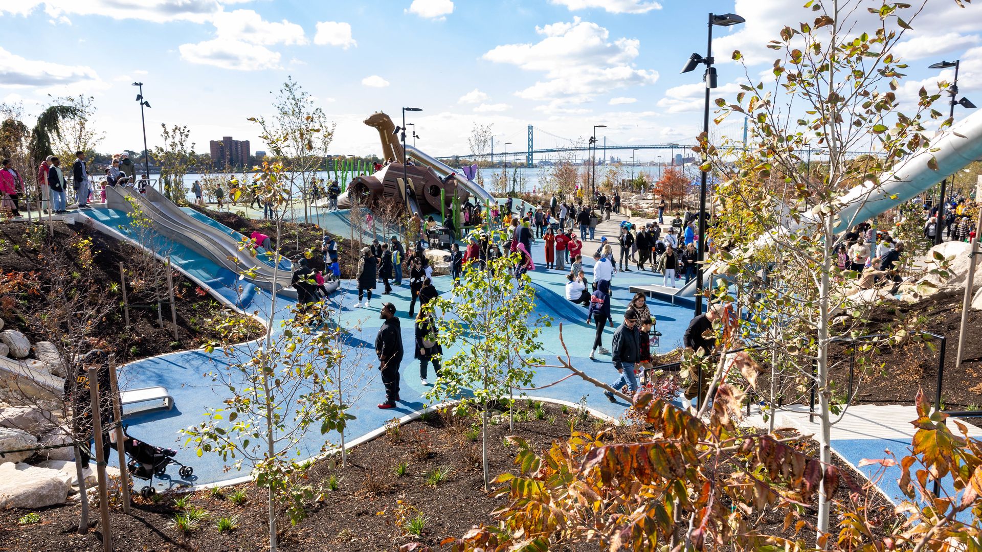 Crowded outdoor playground with slides, trees and safety flooring near the Detroit River and Ambassador Bridge