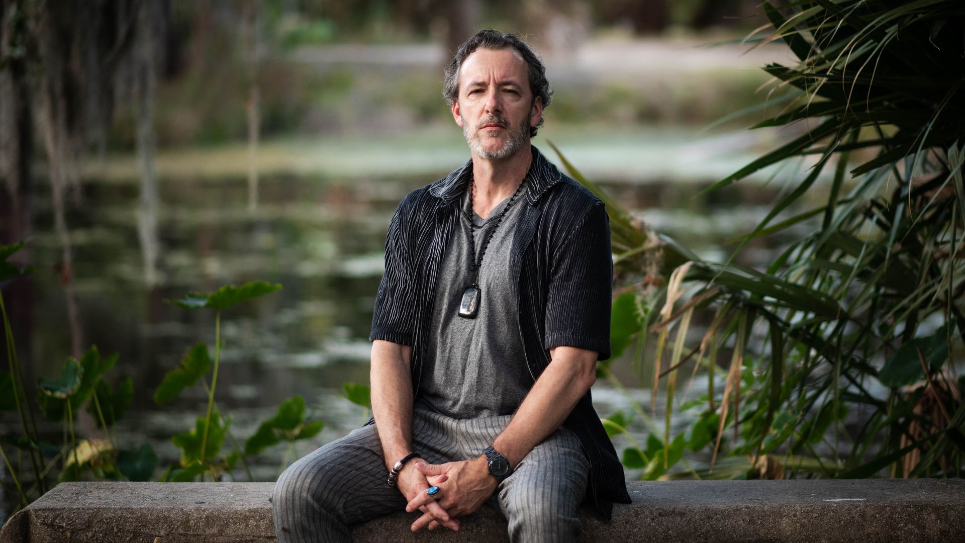 Michael Allen Zell poses for a photo while sitting on a bench in a swampy area. 