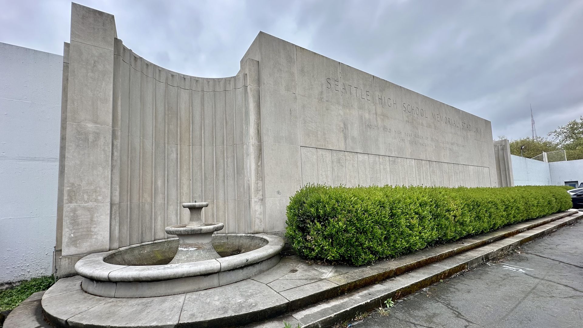 The memorial wall at Seattle's Memorial Stadium with a dry fountain in the front and a bush alongside the wall.