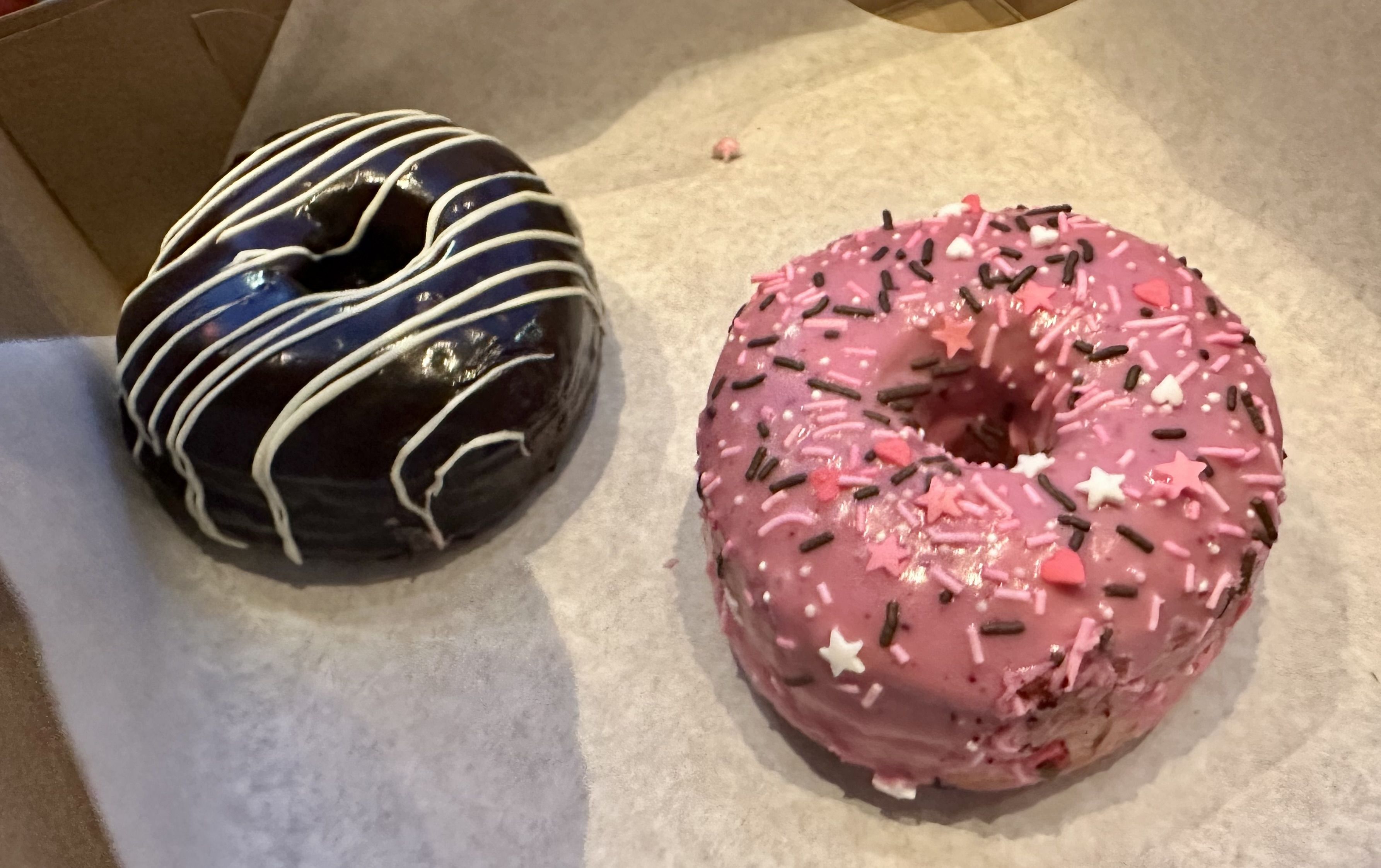 A chocolate frosted doughnut with white frosted stripes next to a pink sprinkle doughnut with pink frosting.