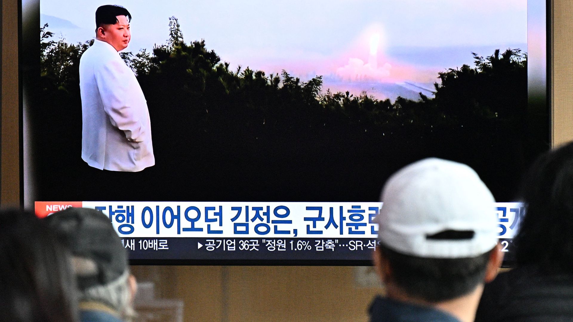 People sit near a television showing a news broadcast with file footage of North Korean leader Kim Jong Un overseeing a missile test, at a railway station in Seoul on October 10.