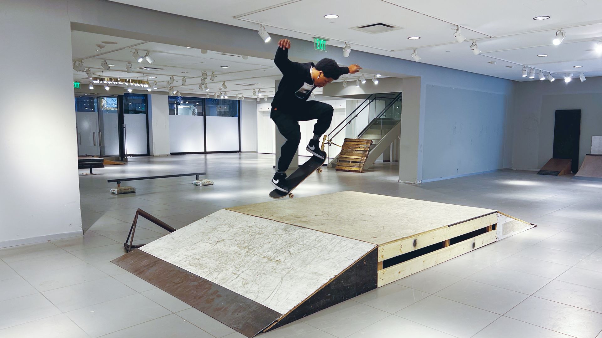 A skateboarder does a trick on a ramp in a vacant store.