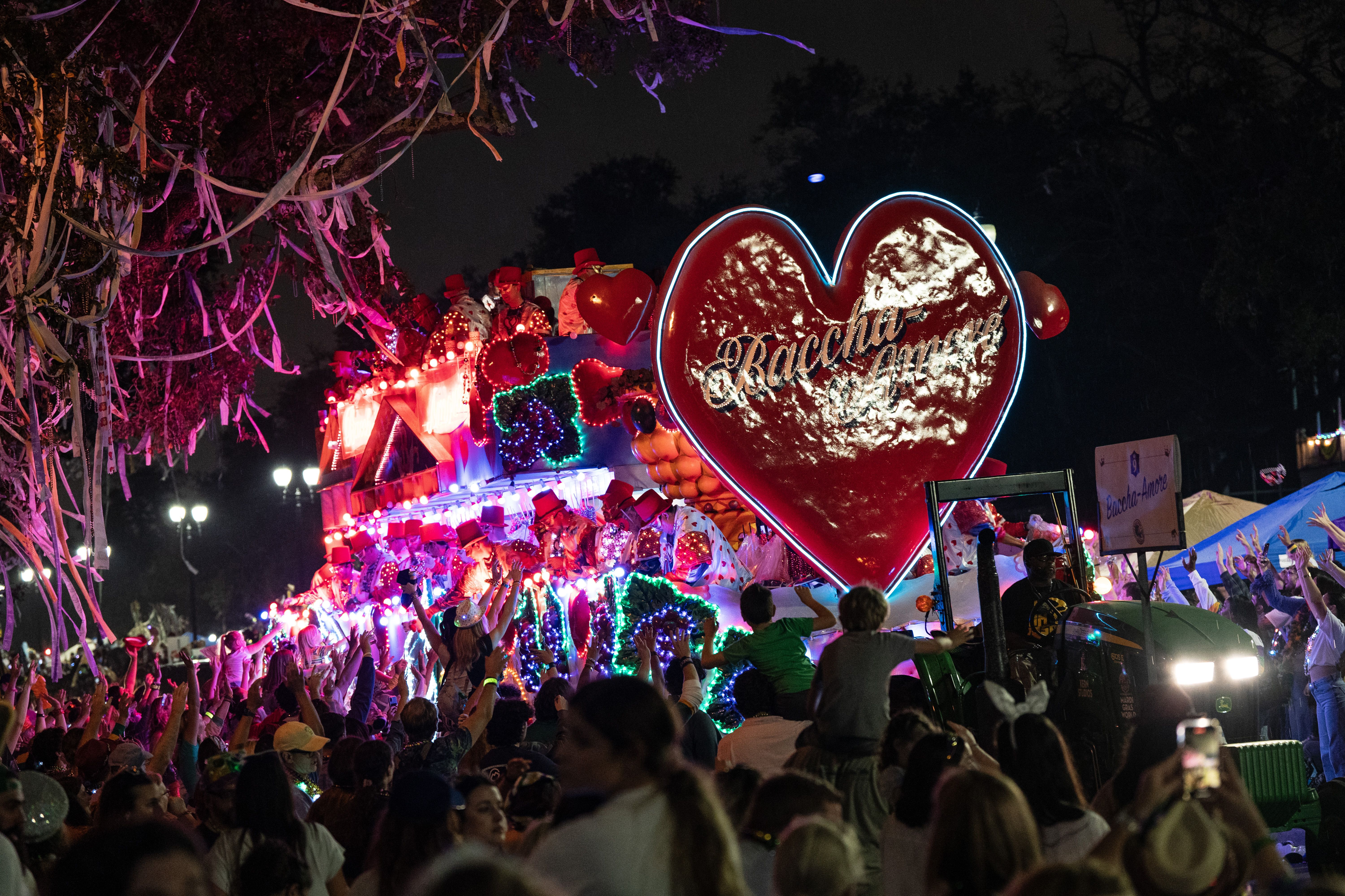 A Mardi Gras float with a large heart on the front comes down the route. The heart says Baccha-Amore.