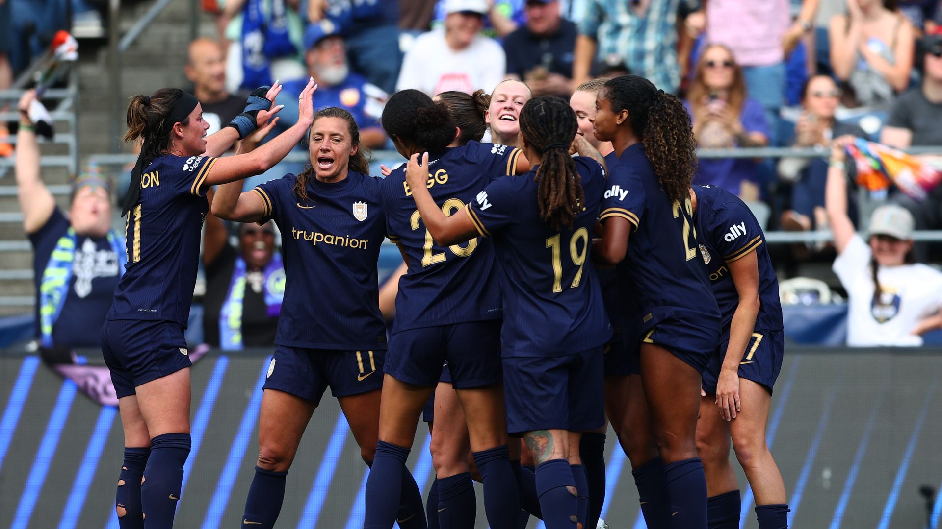 Seattle Reign players gather in a jubilant group celebration on the field during a match against the Houston Dash.