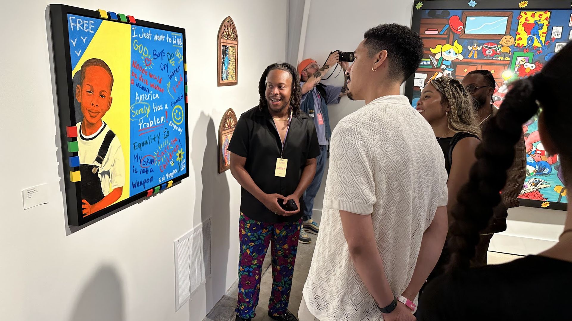 Gallery scene with people viewing colorful art: left a portrait of a boy in overalls against blue and yellow; center a smiling man in a black shirt with a badge; others watch, with more murals in the back.