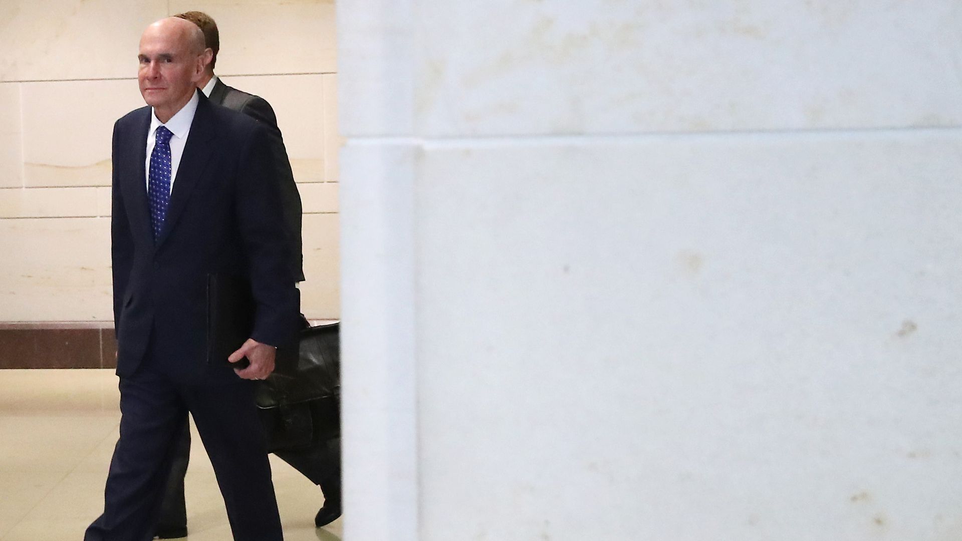 In this image, McKinley walks in a suit around a corner with another suited man behind him