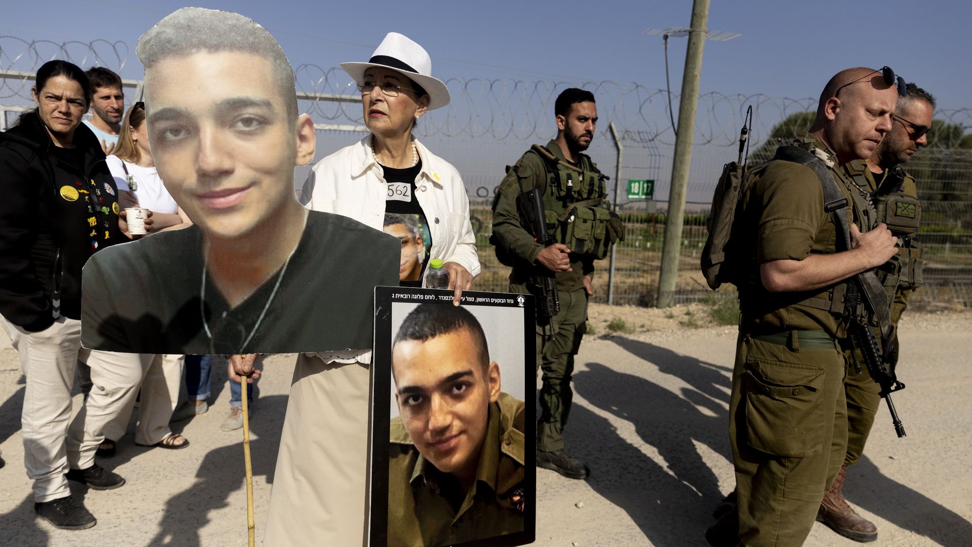 Varda Ben Baruch holds photos of her grandson Israeli- American hostage Edan Alexander as she walks near Israeli soldiers during a rally of families of hostages held in the Gaza Strip at Nir Oz near the border with the Gaza Strip on April 20, 2025 in Nir Oz, Israel. Family